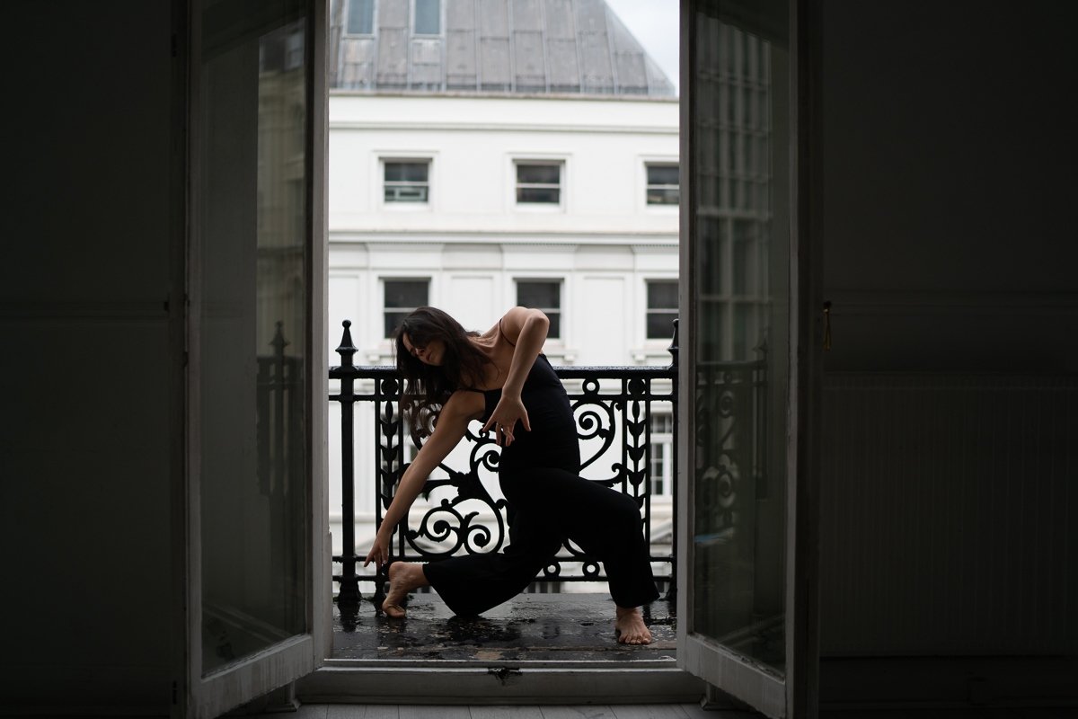 Sarah Hirsch reaching down from a sunlit balcony