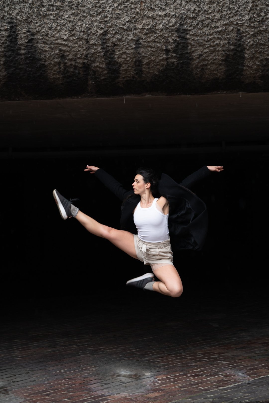 Sarah Hirsch performing a grand jeté in a dark studio, blazer flying mid-air